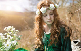 A cute red-haired girl in a green dress with a wreath on her head