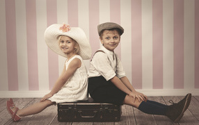 Девочка в большой белой шляпе и мальчик сидят на чемодане