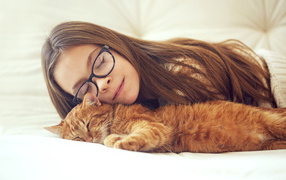 A girl in glasses sleeps with a red cat