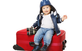 Маленький мальчик в шапке с биноклем сидит на красном чемодане