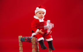 Маленький мальчик сидит на стуле с новогодним подарком