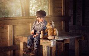 A little boy is sitting on a wooden table with a teddy bear