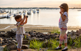 Маленький мальчик фотографирует девочку на берегу