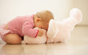 A little child is playing with a pink toy bear