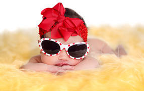 Маленькая забавная малышка в очках и с красным бантом на голове