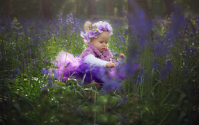 Маленькая девочка в красивом платье сидит в цветах с бабочкой на руке