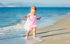 Маленькая девочка в розовом платье гуляет по морскому песку