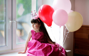 A little girl in a princess costume sits on a window