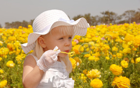 Маленькая девочка в белой шляпе пускает мыльные пузыри на поле с желтыми лютиками