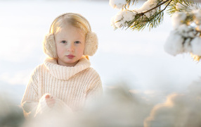 Маленькая девочка в белом свитере у покрытой снегом ели