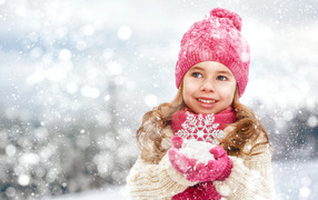 A little girl in winter clothes is holding snow in her hands