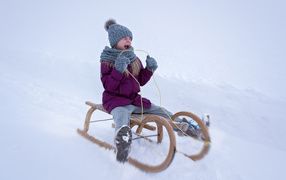 A little girl is riding a sleigh with a roller coaster in the winter