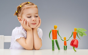 Маленькая девочка сидит за столом с фигурками из овощей