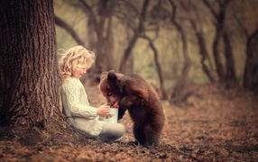 A little girl is sitting at a tree with a grizzly bear