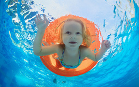 Маленькая девочка плавает в бассейне со спасательным кругом