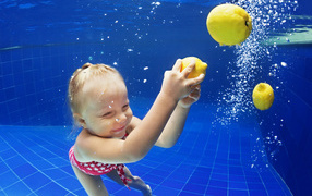 Маленькая девочка плавает в бассейне с желтыми лимонами