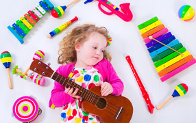 Маленькая девочка с гитарой лежит рядом с детскими музыкальными инструментами