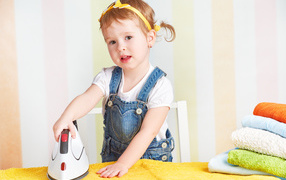 Маленькая девочка с утюгом гладит полотенце