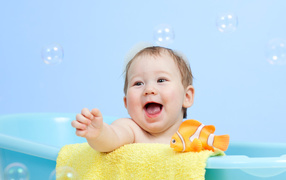 Веселый малыш купается в ванной с игрушечной рыбкой