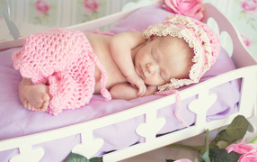A sleeping baby girl in a pink suit in a cradle