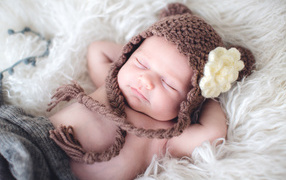 Спящий грудной ребенок в коричневой вязаной шапке с белым цветком