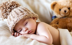 A sleeping baby in a hat with a teddy bear
