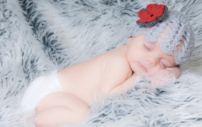 Спящий грудной ребенок в вязаной шапке с красным цветком на голове