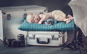 Спящий младенец с фотоаппаратом спит на чемодане