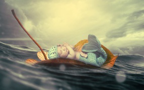 A small baby in a mermaid costume floats on a sheet in the ocean