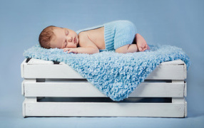 Маленький грудной ребенок спит на синем покрывале на деревянном ящике
