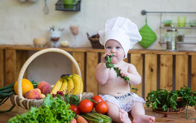 Маленький ребенок в шапке повара сидит на столе с овощами