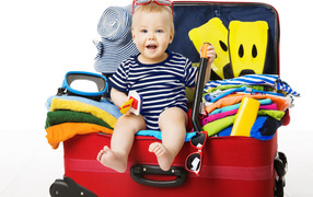 Маленький ребенок сидит в большом красном чемодане с вещами