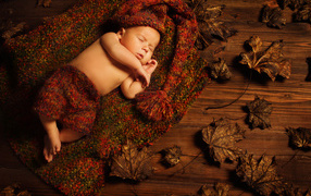A small child sleeps in a knitted suit on the floor with dry leaves