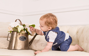 Маленький ребенок рассматривает цветы в железной лейке