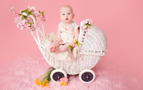 Младенец девочка сидит в коляске на розовом фоне