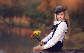 Красивая девочка в кепке с букетом в руках сидит на дереве