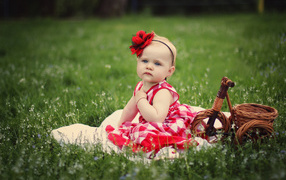Красивая маленькая девочка с красным цветком на голове сидит на зеленой траве