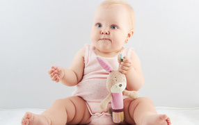 Голубоглазый младенец с мягкой игрушкой на сером фоне