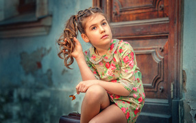 Кареглазая девочка в цветастом платье сидит на пороге