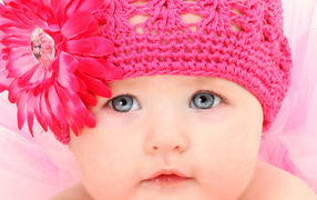 Милая голубоглазая малышка в розовой шапке с цветком герберы