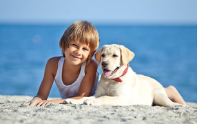 Симпатичный мальчик со щенком ретривера лежат на песке на пляже