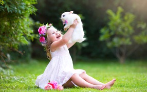 Joyful little girl in white dress with rabbit in hands