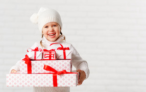 Смеющаяся девочка в белой шапке с новогодними подарками