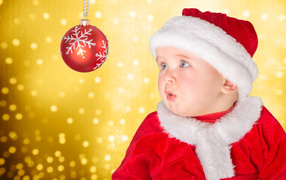 Little baby boy in Santa costume looks at Christmas ball
