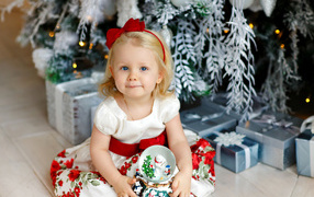Little blonde girl sits with presents under Christmas tree