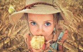 Маленькая голубоглазая девочка в шляпе ест яблоко