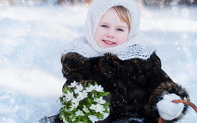 Little blue-eyed girl with a bouquet of snowdrops in winter