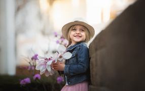 Маленькая голубоглазая улыбающаяся девочка в шляпе с букетом в руках
