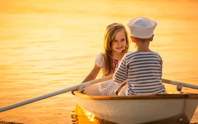 Маленькие мальчик и девочка плывут в лодке на закате солнца