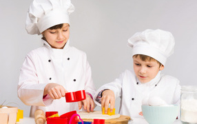 Маленькие мальчик и девочка готовят на кухне печенье